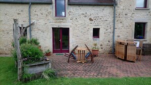 A stone building with a red door, a small window, and a brick patio with outdoor furniture. - Bed and Breakfast 'Chambre D'hôtes Bois De Rose' with Private Garden and Wi-Fi (La Hoguette)