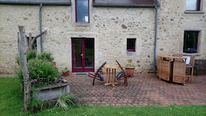 A stone building with a red door, a small window, and a brick patio with outdoor furniture. - Bed and Breakfast 'Chambre D'hôtes Bois De Rose' with Private Garden and Wi-Fi (La Hoguette)