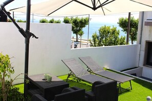 An outdoor patio with two lounge chairs, a table, and a large umbrella. - The Casa da Fonteseca Wake up facing the sea (Ribeira)