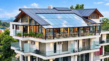 A multi-story building with a rooftop solar panel array, outdoor seating area, and multiple balconies.