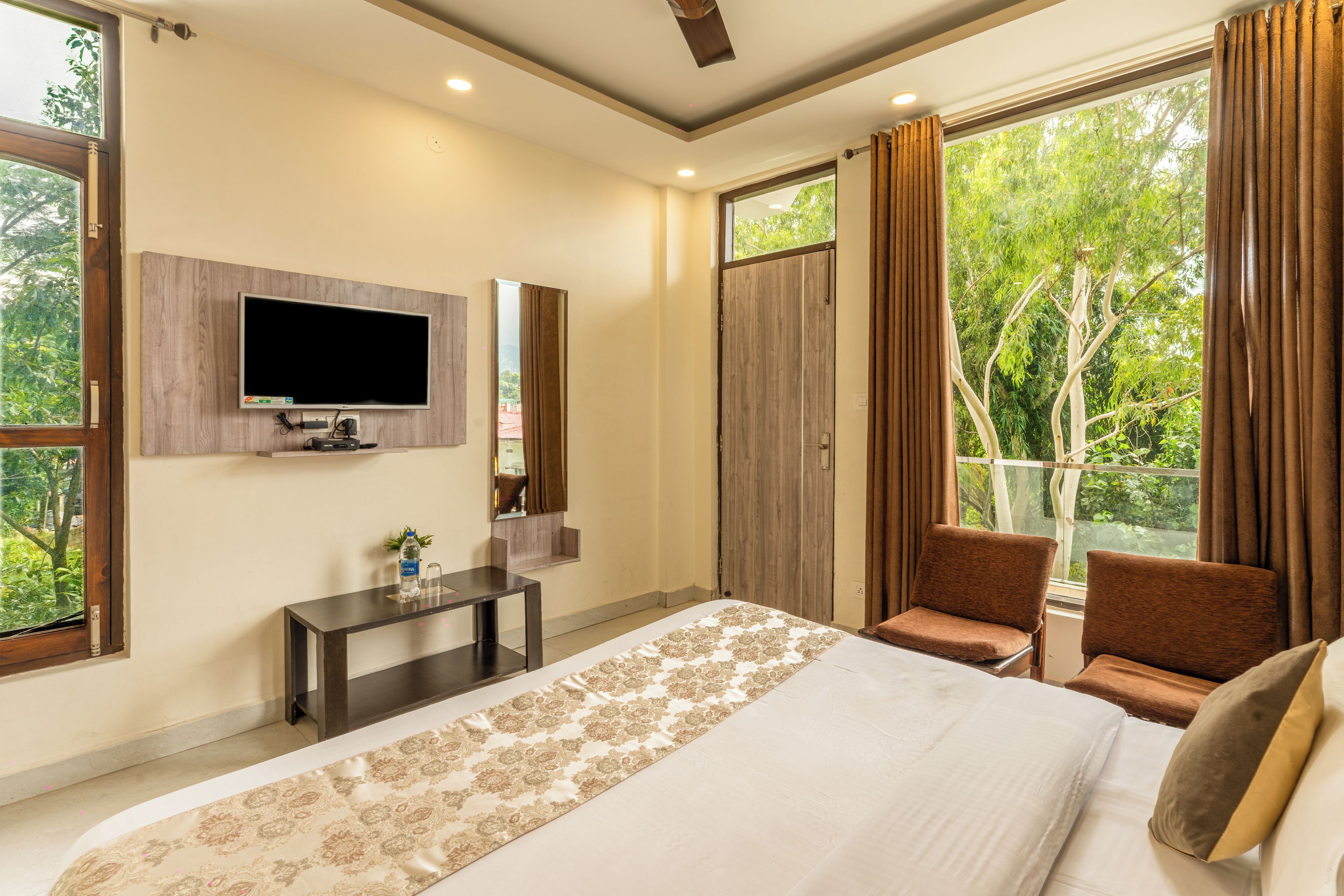 Un dormitorio con cama, televisor, escritorio y balcón con cortinas.