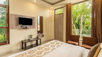 Un dormitorio con cama, televisor, escritorio y balcón con cortinas.