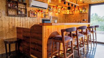 Una zona de bar con mostrador, taburetes y estantes llenos de botellas.