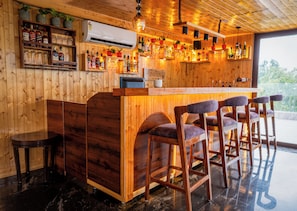 Una zona de bar con mostrador, taburetes y estantes llenos de botellas.