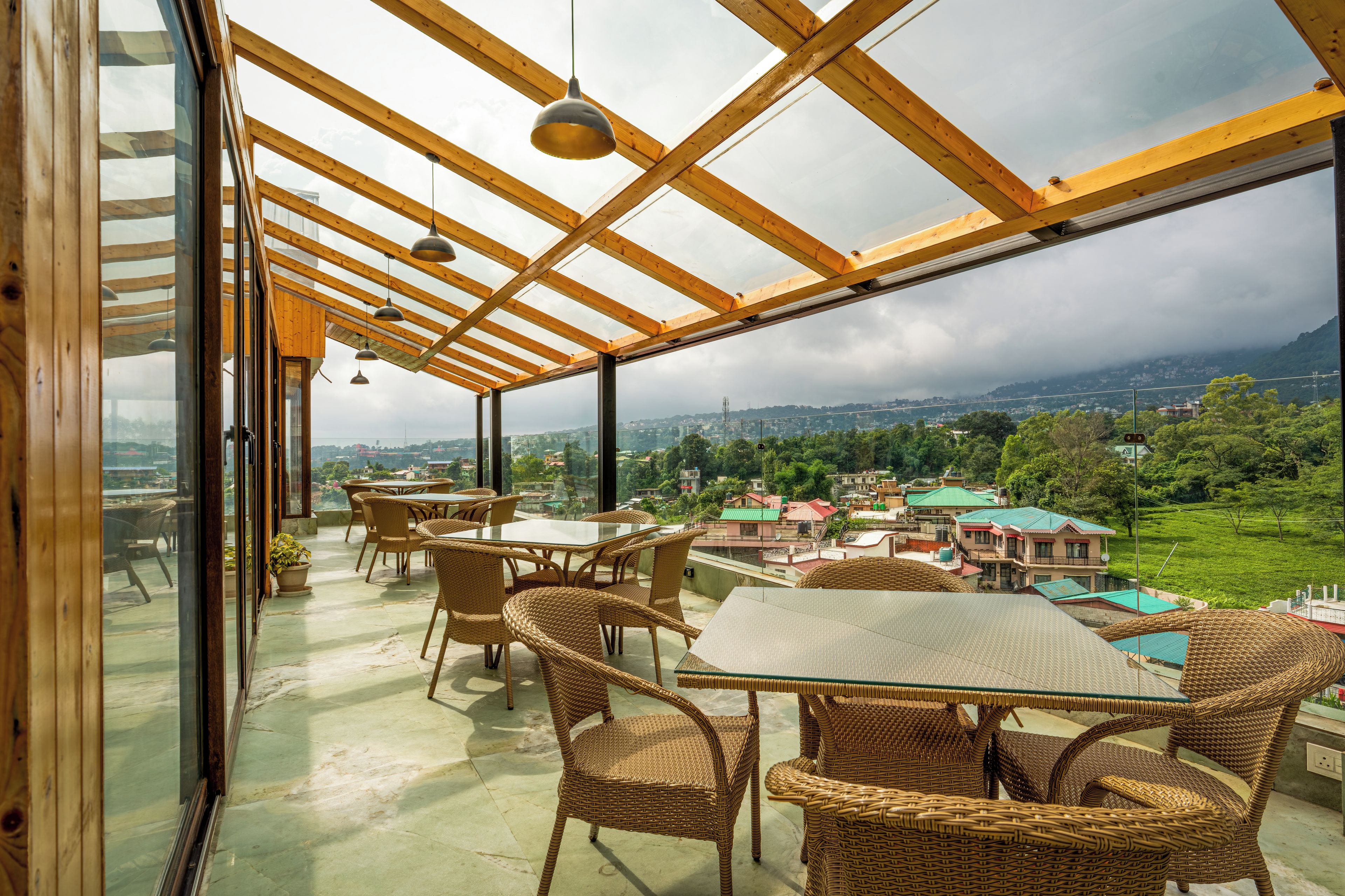 Ein geräumiger Balkon mit Korbmöbeln und einem Glastisch, mit Blick auf eine reizvolle Landschaft mit Gebäuden und viel Grün.