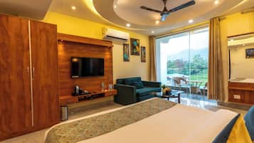 A hotel room with a large bed, a TV mounted on a wooden panel, a sofa, a small table, and a balcony with a view.