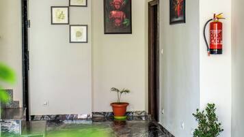 A hallway with a marble floor, framed artwork on the walls, a potted plant, and a fire extinguisher.