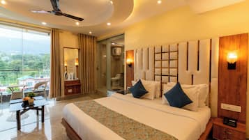 Une chambre d’hôtel avec un grand lit, une table de chevet, un bureau avec une chaise, une salle de bain avec une porte en verre et une vue sur l’extérieur.