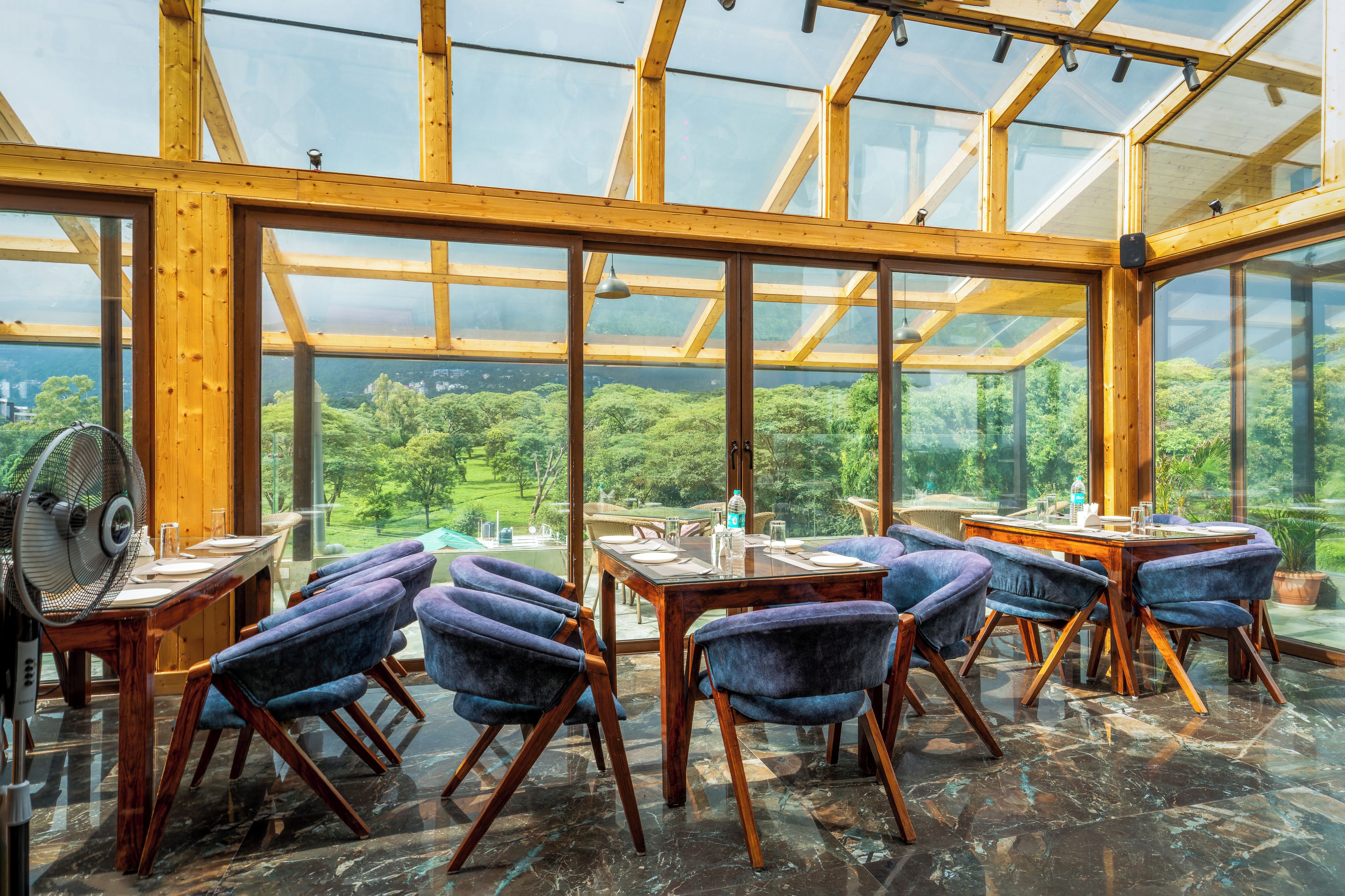 Un restaurant doté d’un plafond en verre, de poutres en bois et offrant une vue sur la forêt.