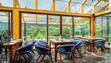 Un restaurant doté d’un plafond en verre, de poutres en bois et offrant une vue sur la forêt.