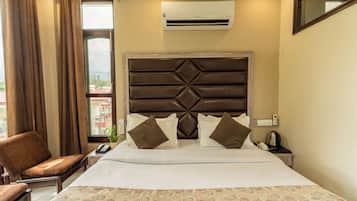 Habitación de hotel con cama, una silla, unidad de aire acondicionado, mesita de noche y ventana con cortinas.