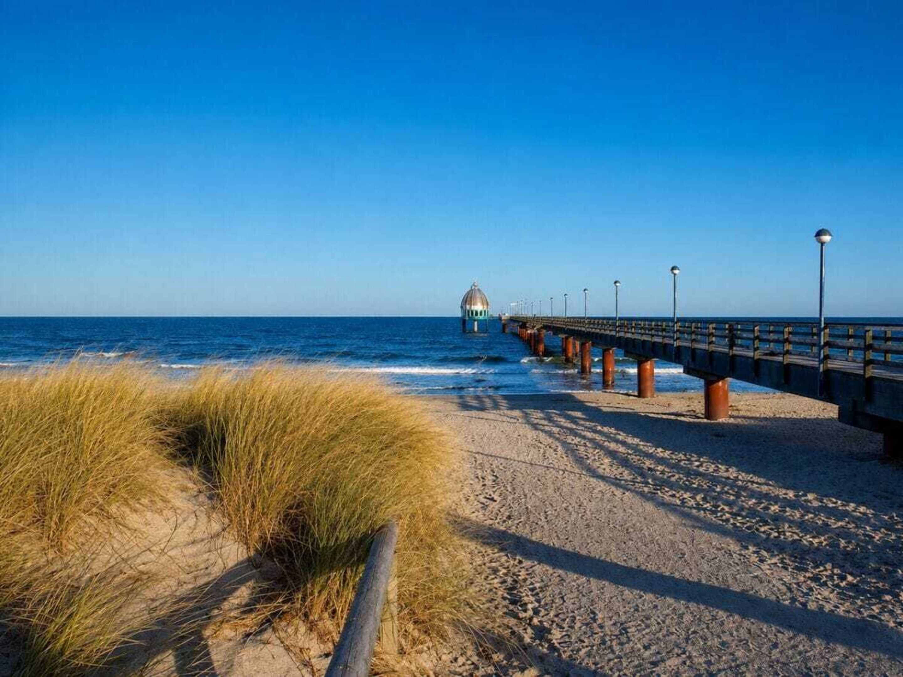 A beach with a wooden pier extending into the sea, featuring a dome structure at the end.