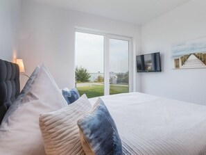 Ein Schlafzimmer mit Bett, Fernseher und Fenster mit Blick auf Wasser und Grünflächen.