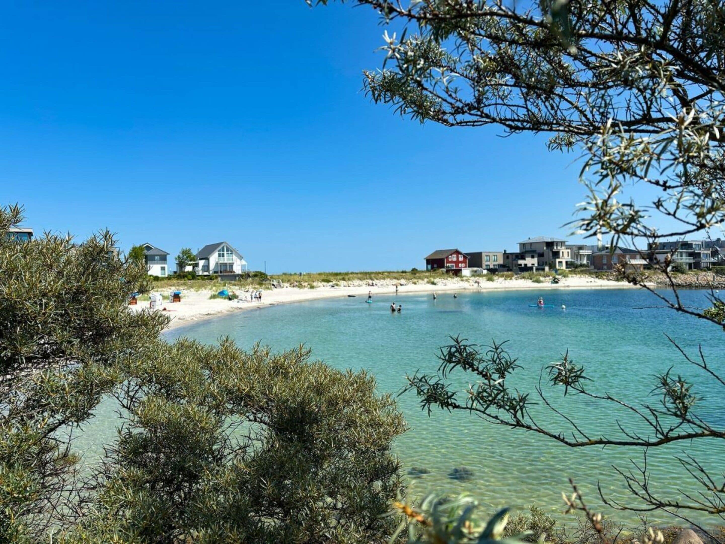 Eine Küstenlandschaft mit klarem, blauem Wasser, einem Sandstrand und Gebäuden entlang der Uferlinie.