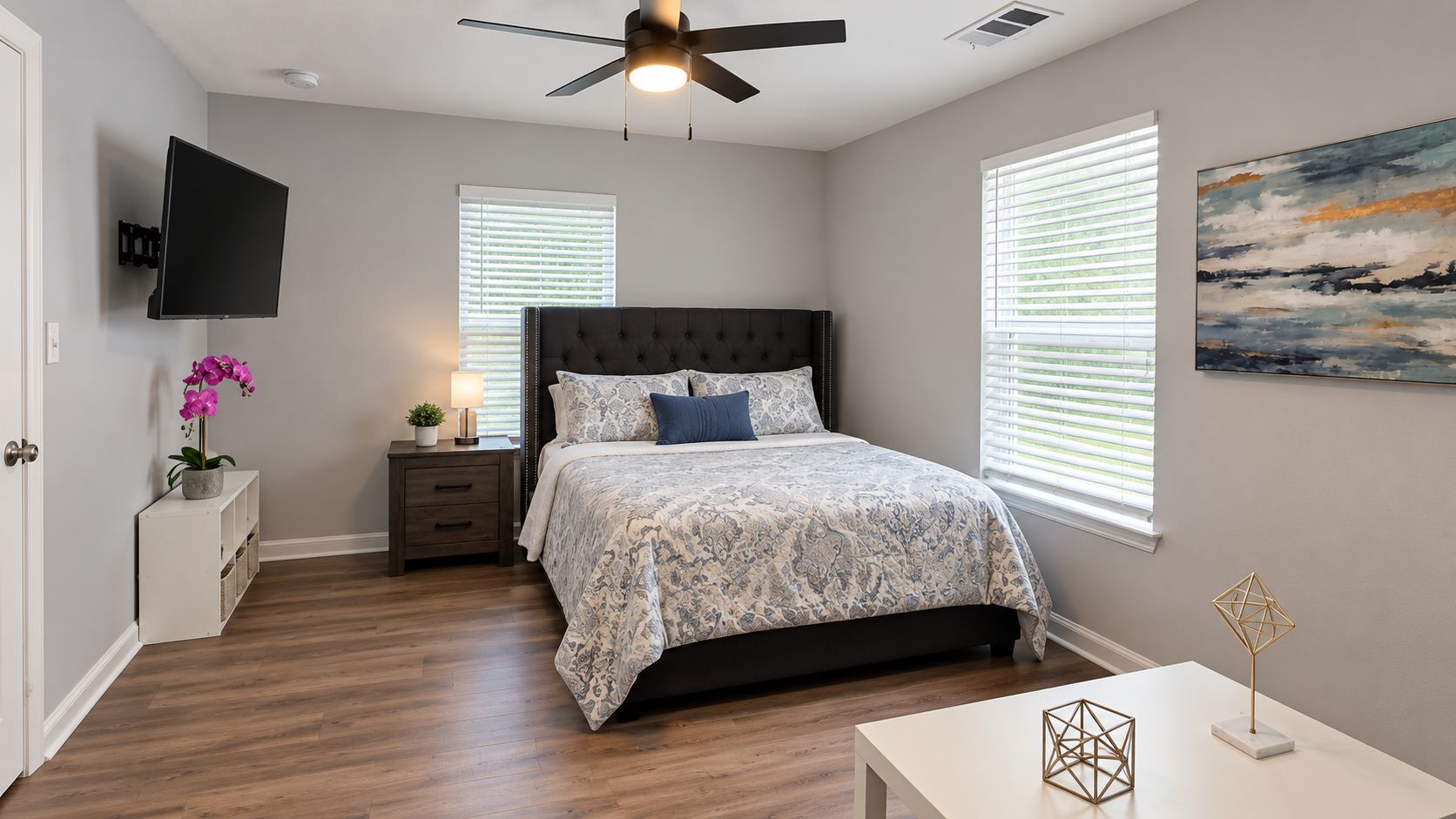 A bedroom with a bed, bedside table, nightstand, TV, and artwork on the wall.