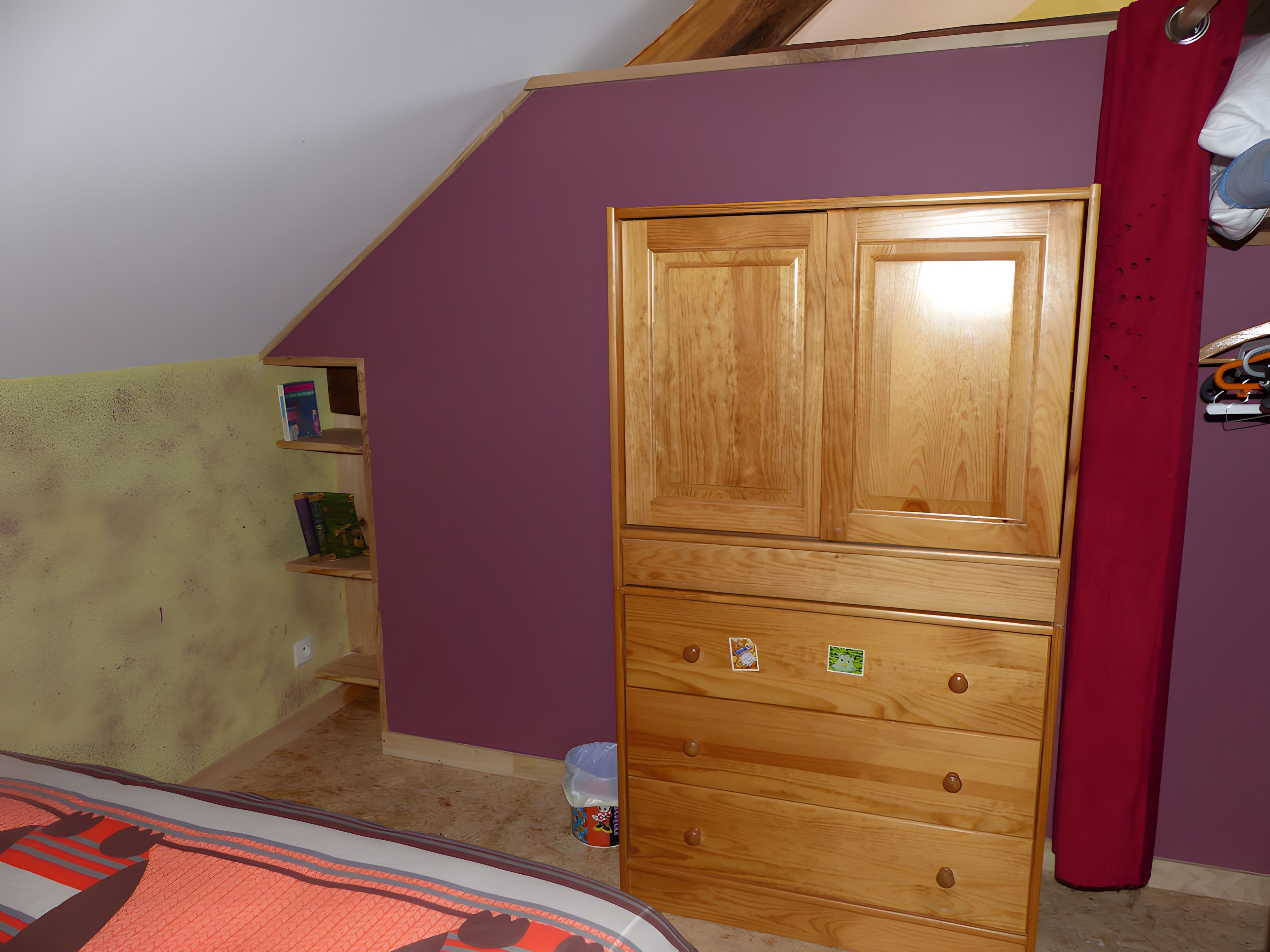 Une pièce avec une armoire en bois, un mur violet et un rideau rouge.