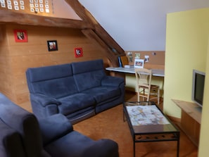 Una sala acogedora con un sofá azul, techo de madera y una pequeña mesa con papeles.