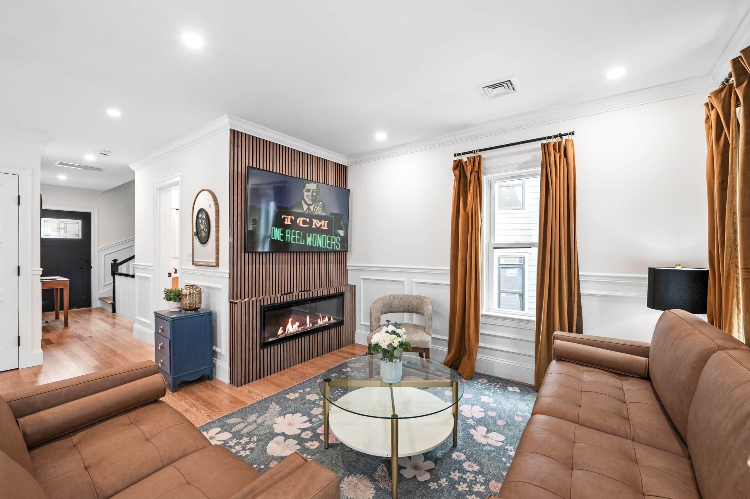 A modern living room with a fireplace, a television mounted on the wall, and a seating area with two sofas.