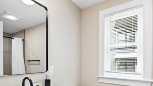 Een moderne badkamer met een wit wastafel, een zwarte kraan en een houten kastje. Er is een toilet en een raam met zonwering.