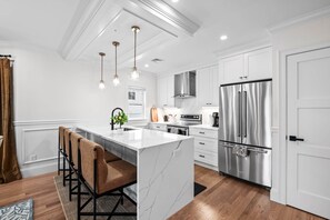 A modern kitchen with a central island, stainless steel appliances, pendant lighting, and a view to the dining area. - Designer Condo in Jamaica Plain | Steps to Forest Hills (Boston)