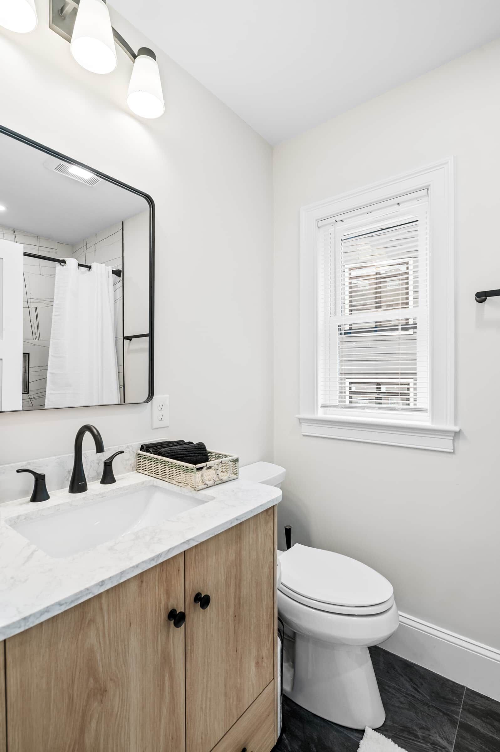 A modern bathroom with a white vanity, black faucet, and a wooden cabinet.