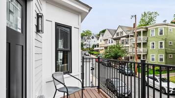 A wooden deck with a chair, a black metal railing, and a view of a street with houses.