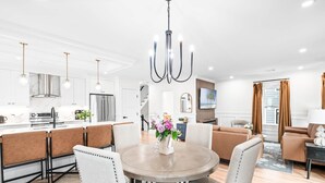 Een moderne keuken met roestvrijstalen apparatuur, een eetruimte met een ronde tafel en stoelen, en een woonkamer met een bank en een televisie.