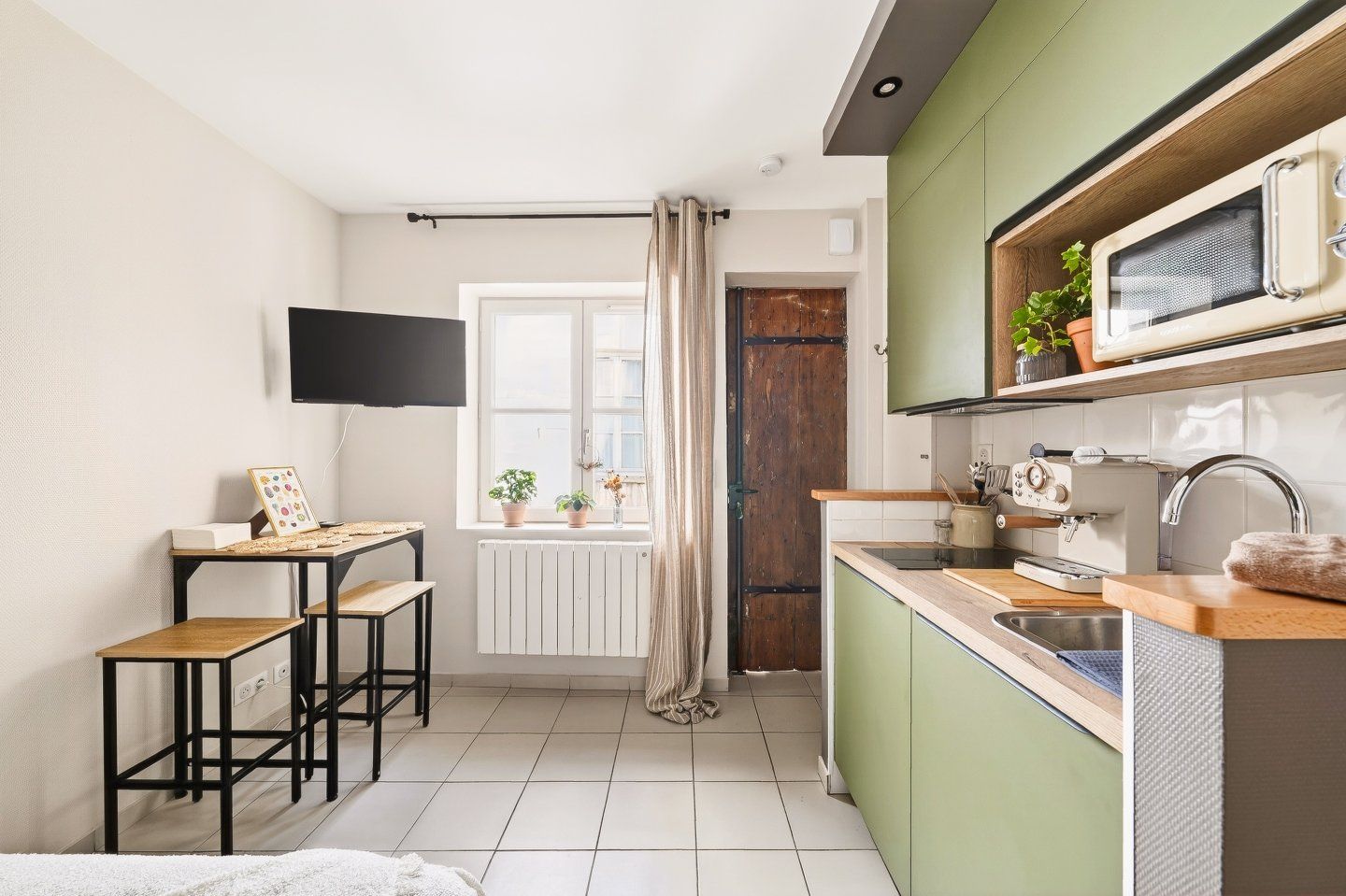 Een functionele keuken met een magnetron, spoelbak en een klein eethoekje met krukjes.