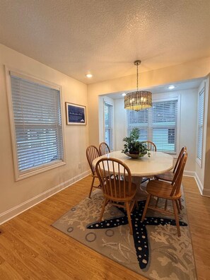 A dining area with a round table, wooden chairs, a chandelier, and a patterned rug. - Short Walk to Beach, Cozy Stay in Ocean Lakes (Myrtle Beach)
