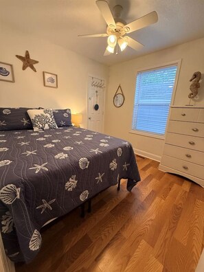 A bedroom with a bed, a ceiling fan, a dresser, and a window with blinds.
