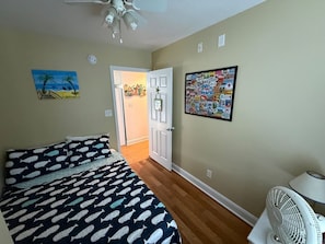 A bedroom with a bed, a door, a wall with a poster, and a fan. - Short Walk to Beach, Cozy Stay in Ocean Lakes (Myrtle Beach)