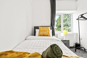 A bedroom with a bed, a bedside table, a lamp, and a window with curtains. - Spacious 5 Bedrooms 2.5 Bathrooms | 8 Beds | WiFi | Driveway | Atherton M46 (Atherton)