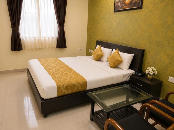 Una habitación de hotel con cama, mesita de noche, silla y una mesa con superficie de vidrio.
