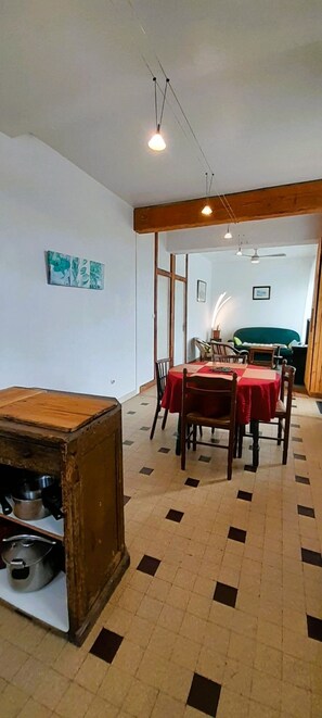 A dining area with a table set for four, a wooden cabinet with kitchenware, and a hallway leading to a green sofa. - La Forge- Gite 4 pers- face au canal du Berry- Wifi (Thénioux)