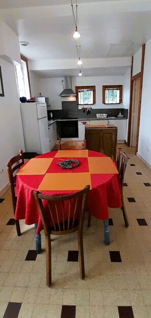 A dining area with a table set for four, a kitchen in the background, and a tiled floor. - La Forge- Gite 4 pers- face au canal du Berry- Wifi (Thénioux)