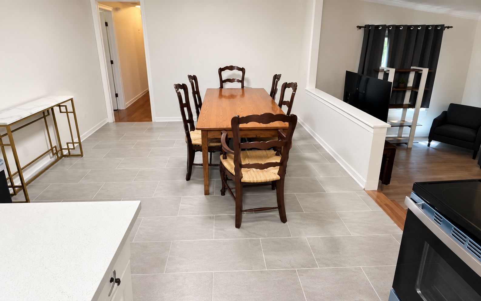 A dining area with a wooden table and chairs, a kitchen with a stove, and a living area with a couch and TV.