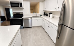 A modern kitchen with stainless steel appliances, white cabinetry, and a tiled floor.