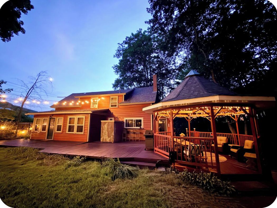 A wooden house with a covered porch and a gazebo with lights.