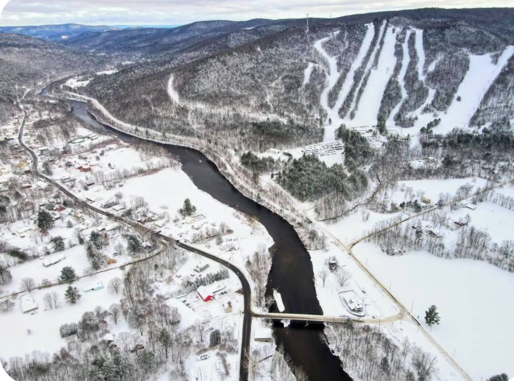 A river winding through a snowy landscape with a bridge and buildings on the riverbank.