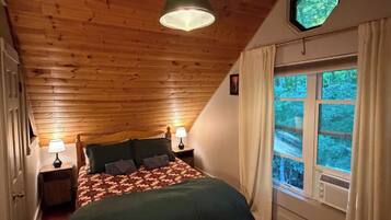 A bedroom with a wooden ceiling, a bed with a patterned blanket, two bedside lamps, and a window with curtains.