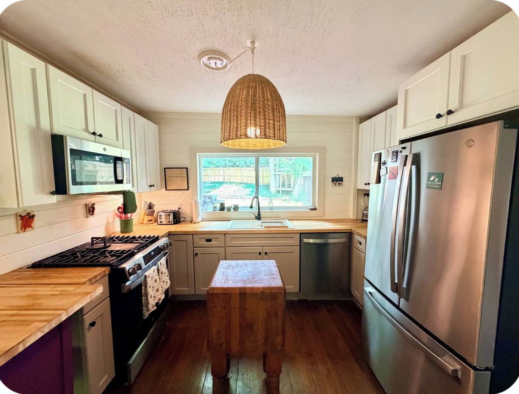 A kitchen with white cabinets, stainless steel appliances, a wooden countertop, and a hanging light fixture.