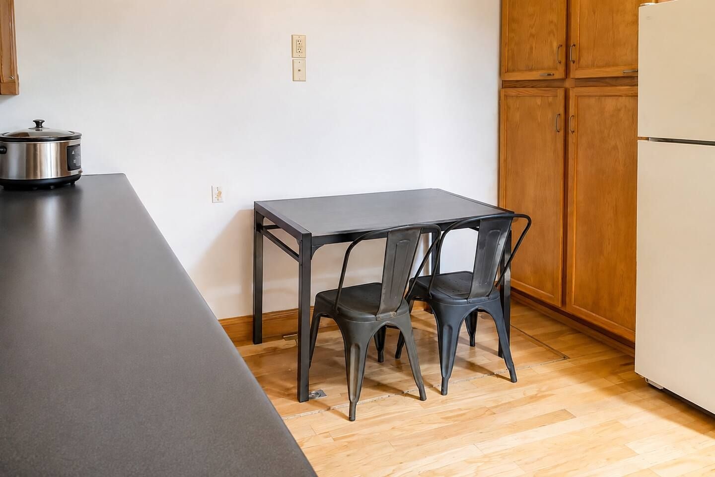 A kitchen with a black table and two chairs, a stove, and wooden cabinets.