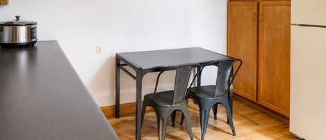 A kitchen with a black table and two chairs, a stove, and wooden cabinets.
