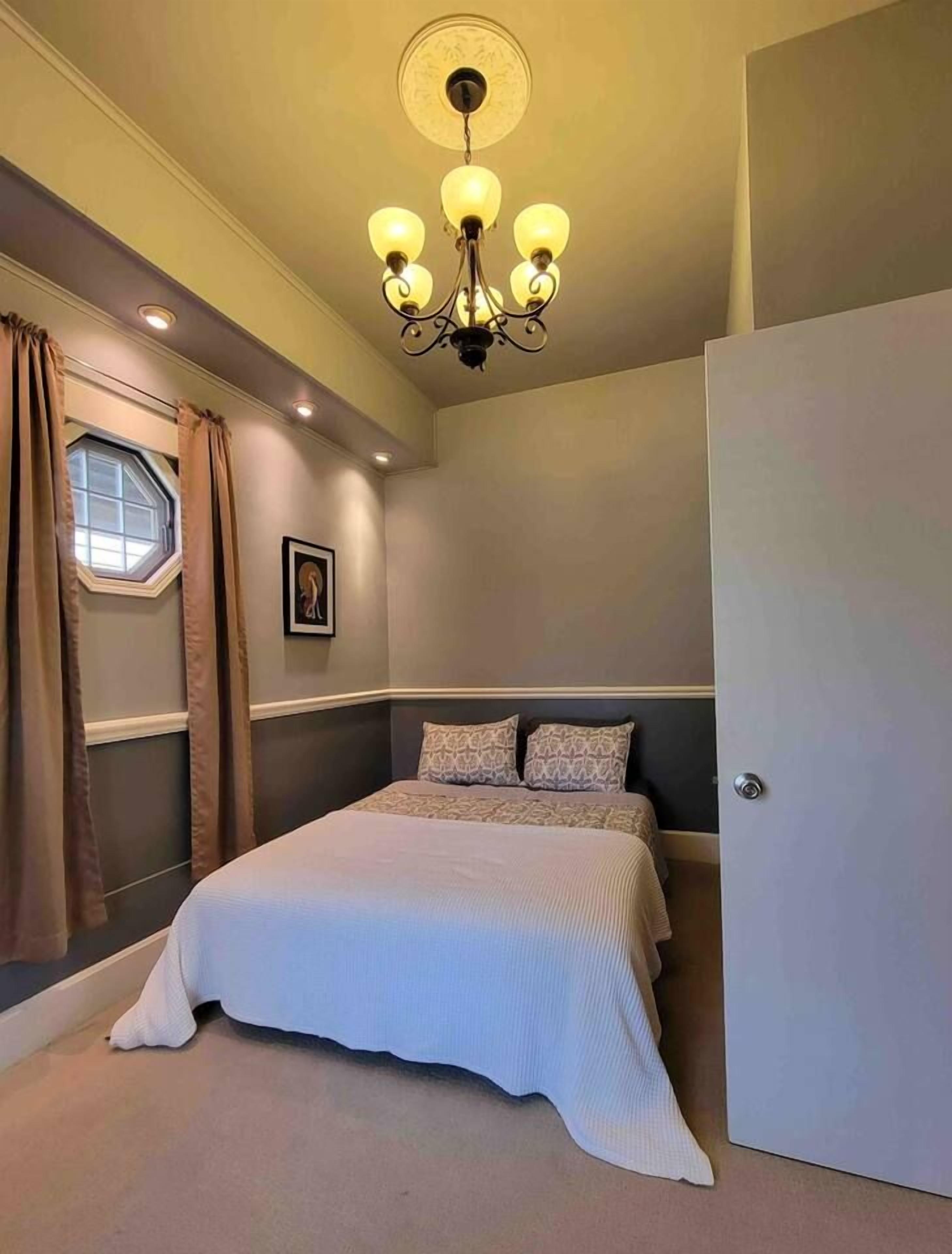 Un dormitorio con una cama, un candelabro, una ventana con cortinas y una puerta.