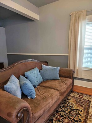 A brown leather sofa with decorative pillows, a patterned rug, and a window with curtains. - Cozy 2BR Indianapolis Home | Pet Friendly (Indianapolis)