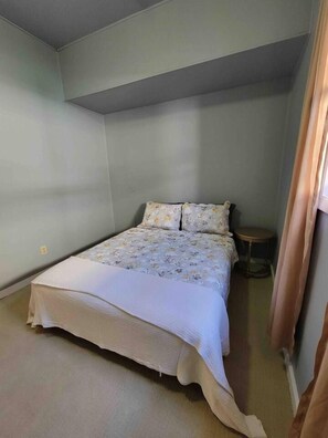 A small, single-bed room with a plain wall and a small round table. - Cozy 2BR Indianapolis Home | Pet Friendly (Indianapolis)