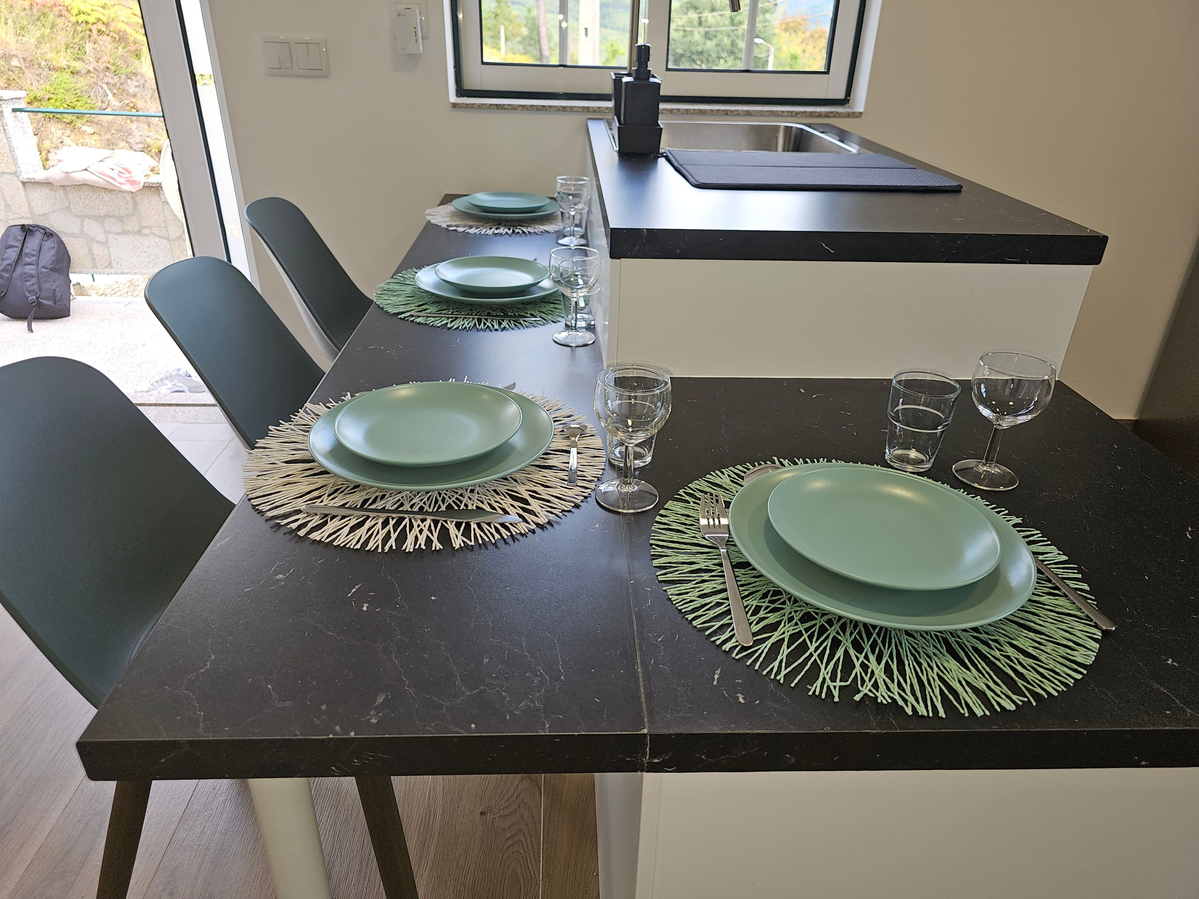 A dining table set with green plates, clear glasses, and a black countertop with a sink.
