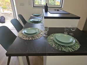 A dining table set with green plates, clear glasses, and a black countertop with a sink. - Holiday Home with Beautiful Views near Gerês Park, Private Terrace, Wi-Fi & Air Conditioning (Lindoso)