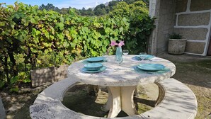 A round stone table with a bench, set outdoors with a view of a vineyard in the background.