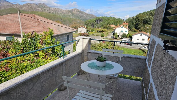 A balcony with a white table and chair, a potted plant, and a view of houses and mountains.